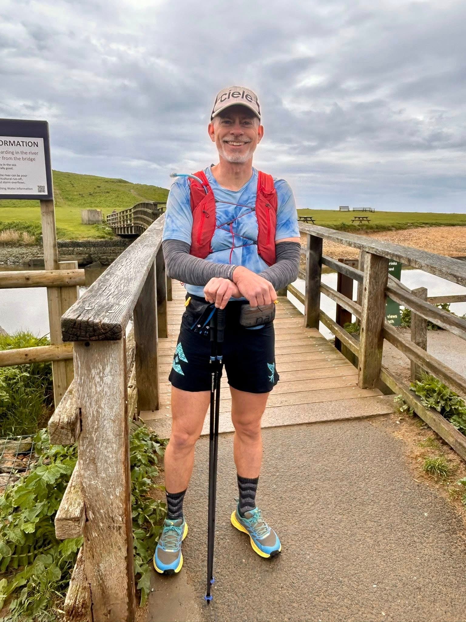 Rich Cowler crossing a wooden bridge on the UK coast with trekking poles
